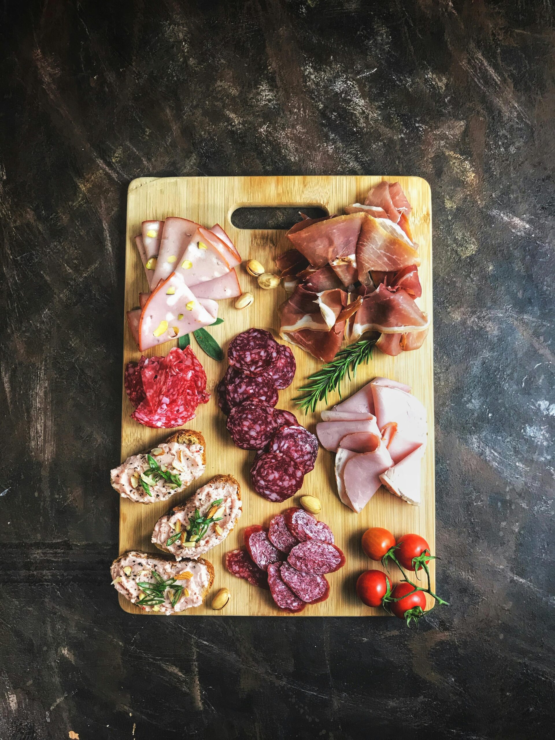 Delicious selection of cold cuts and bread on a wooden board with fresh herbs and tomatoes.